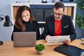 Middle age man and woman business workers using laptop reading document at office