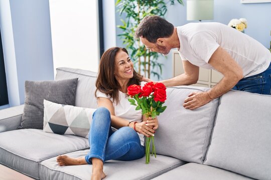 Middle age man and woman couple surprise with flowers sitting on sofa at home - Powered by Adobe