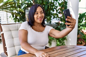 Hispanic brunette woman sitting taking selfie at the terrace