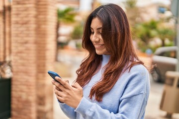 Young hispanic woman smiling confident using smartphone at street