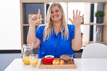Caucasian plus size woman eating breakfast at home showing and pointing up with fingers number seven while smiling confident and happy.