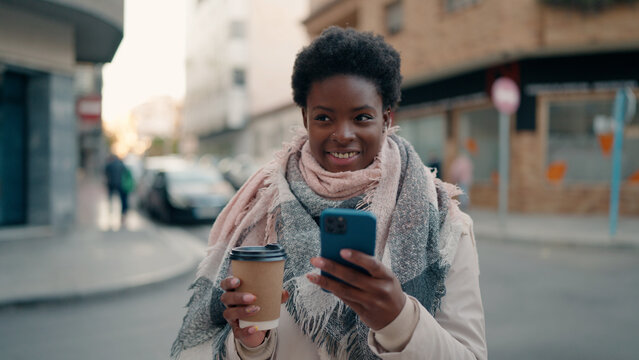 Young african american woman using smartphone drinking coffee at street
