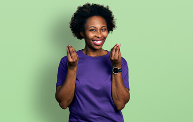 African american woman with afro hair wearing casual purple t shirt doing money gesture with hands,...