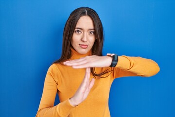 Fototapeta na wymiar Young brunette woman standing over blue background doing time out gesture with hands, frustrated and serious face