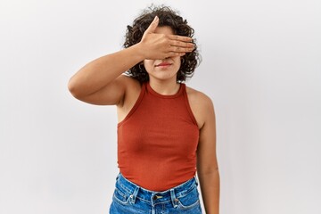 Young hispanic woman wearing glasses standing over isolated background covering eyes with hand, looking serious and sad. sightless, hiding and rejection concept