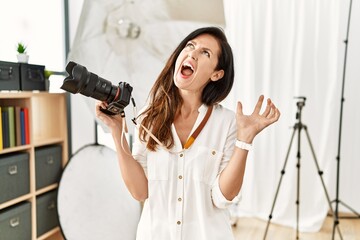 Beautiful caucasian woman working as photographer at photography studio crazy and mad shouting and...