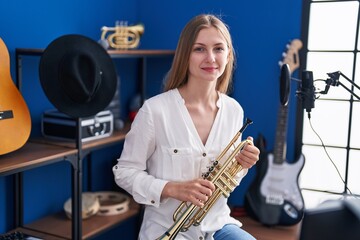 Young caucasian woman musician smiling confident holding trumpet at music studio