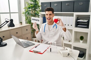 Young hispanic doctor man supporting organs donations celebrating crazy and amazed for success with open eyes screaming excited.