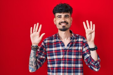 Young hispanic man with beard standing over red background showing and pointing up with fingers...