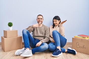 Young couple moving to a new home amazed and smiling to the camera while presenting with hand and pointing with finger.