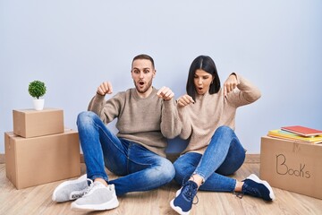 Young couple moving to a new home pointing down with fingers showing advertisement, surprised face and open mouth