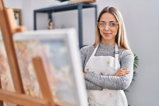 Young woman artist smiling confident standing with arms crossed gesture at art studio