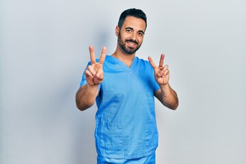 Handsome hispanic man with beard wearing blue male nurse uniform smiling looking to the camera...