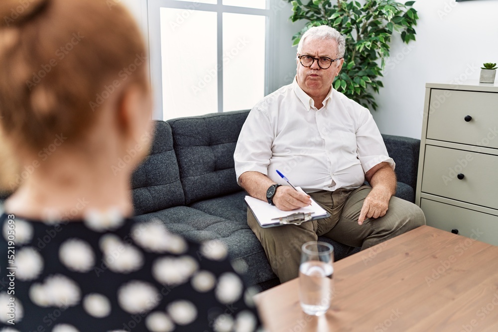 Canvas Prints Senior psychologist man at consultation office puffing cheeks with funny face. mouth inflated with air, crazy expression.