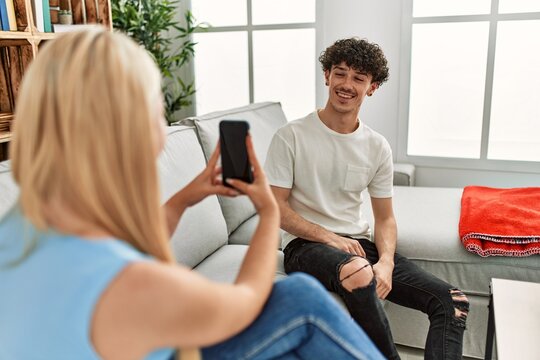 Young woman making picture of her boyfriend using smartphone at home