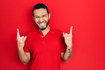 Fototapeta premium Hispanic man with beard wearing casual red t shirt shouting with crazy expression doing rock symbol with hands up. music star. heavy concept.