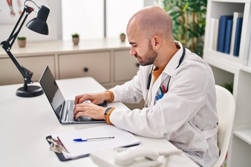 Naklejka na ściany i meble Young man wearing doctor uniform using laptop at clinic