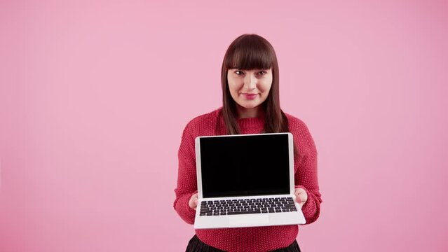 White woman with dark long hair and fringe wearing red sweater and holding laptop computer with black sreen looking at camera. Studio shot. High quality 4k footage