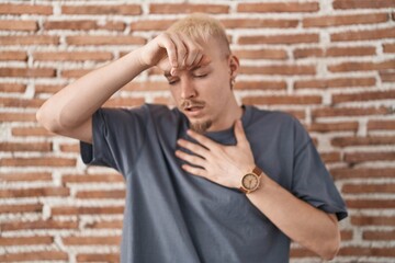 Young caucasian man standing over bricks wall touching forehead for illness and fever, flu and cold, virus sick