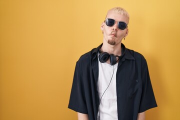 Young caucasian man wearing sunglasses standing over yellow background making fish face with lips, crazy and comical gesture. funny expression.