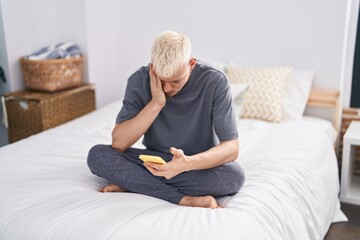 Young caucasian man using smartphone with worried expression at bedroom