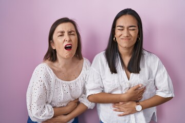 Hispanic mother and daughter together with hand on stomach because indigestion, painful illness...