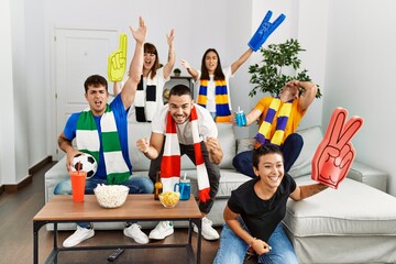 Group of young friends watching and supporting soccer match at home.