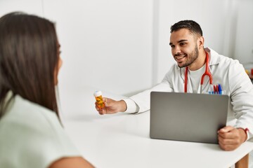 Doctor explain treatment to latin woman using laptop and holding pills at clinic