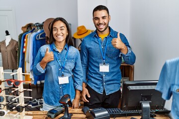 Young interracial people working at retail boutique doing happy thumbs up gesture with hand....