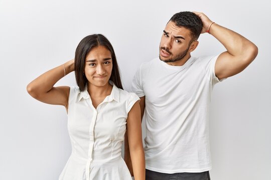 Young interracial couple standing together in love over isolated background confuse and wonder about question. uncertain with doubt, thinking with hand on head. pensive concept.