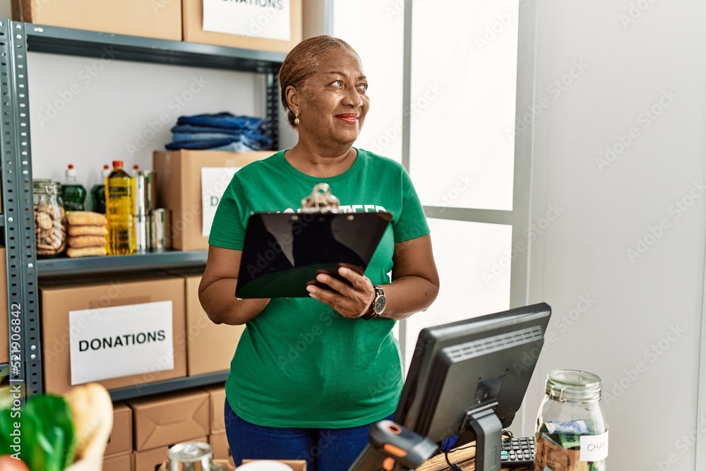 Poster Senior african american woman wearing volunteer uniform writing on clipboard at charity center