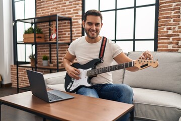 Young hispanic man having online electrical guitar class at home