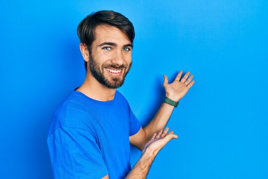Young hispanic man wearing casual clothes inviting to enter smiling natural with open hand