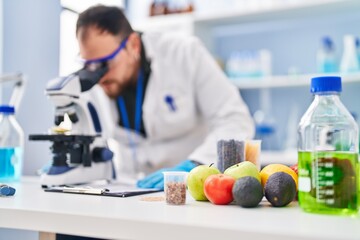 Young hispanic man scientist write on report using microscope at laboratory