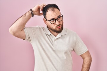 Fototapeta premium Plus size hispanic man with beard standing over pink background confuse and wondering about question. uncertain with doubt, thinking with hand on head. pensive concept.