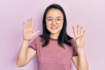 Young chinese girl wearing casual clothes and glasses showing and pointing up with fingers number...