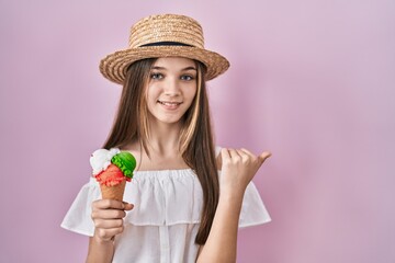 Teenager girl holding ice cream pointing to the back behind with hand and thumbs up, smiling confident