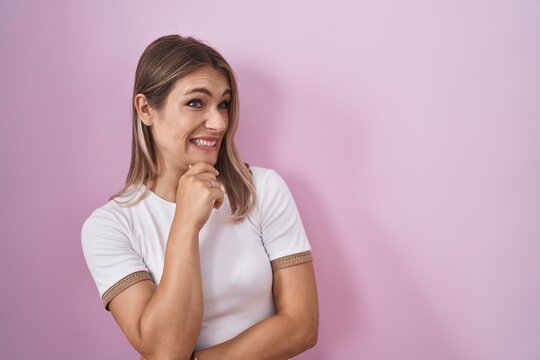 Blonde caucasian woman standing over pink background thinking worried about a question, concerned and nervous with hand on chin