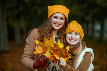 happy mother and child in hats outdoors in city park in autumn