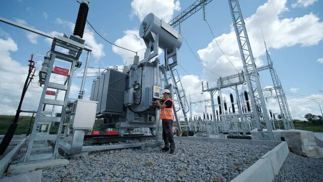 Electrical engineers inspect the electrical systems at the equipment control cabinetю High voltage transformer against the blue sky. Electric current redistribution substation