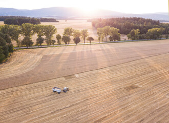 Tractor at wheat field at sunset in countryside mountain lanscape.