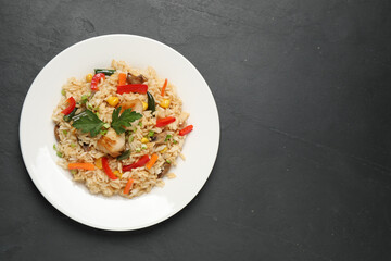 Delicious rice pilaf with chicken and vegetables on black table, top view. Space for text