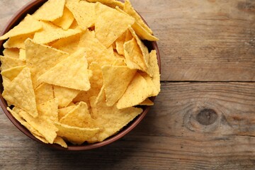 Bowl with tasty tortilla chips (nachos) on wooden table, top view. Space for text