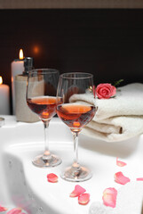 Wine in glasses, towels and rose on edge of bath indoors. Romantic atmosphere