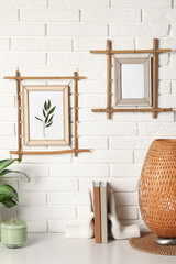 Fototapeta na wymiar Decor elements and books on white table near brick wall with stylish bamboo frames