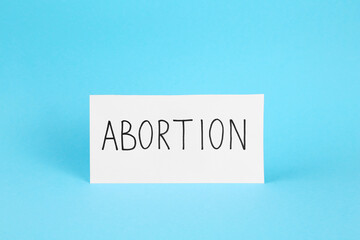 Paper note with word Abortion on light blue background