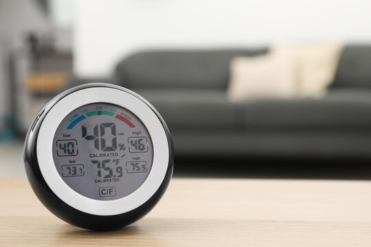 Digital hygrometer with thermometer on wooden table in room. Space for text