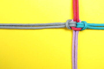 Top view of colorful ropes tied together on yellow background, space for text. Unity concept