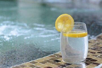 Refreshing water with lemon on edge of swimming pool, space for text
