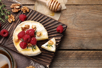 Fototapeta na wymiar Brie cheese served with raspberries, walnuts and honey on wooden table, flat lay. Space for text